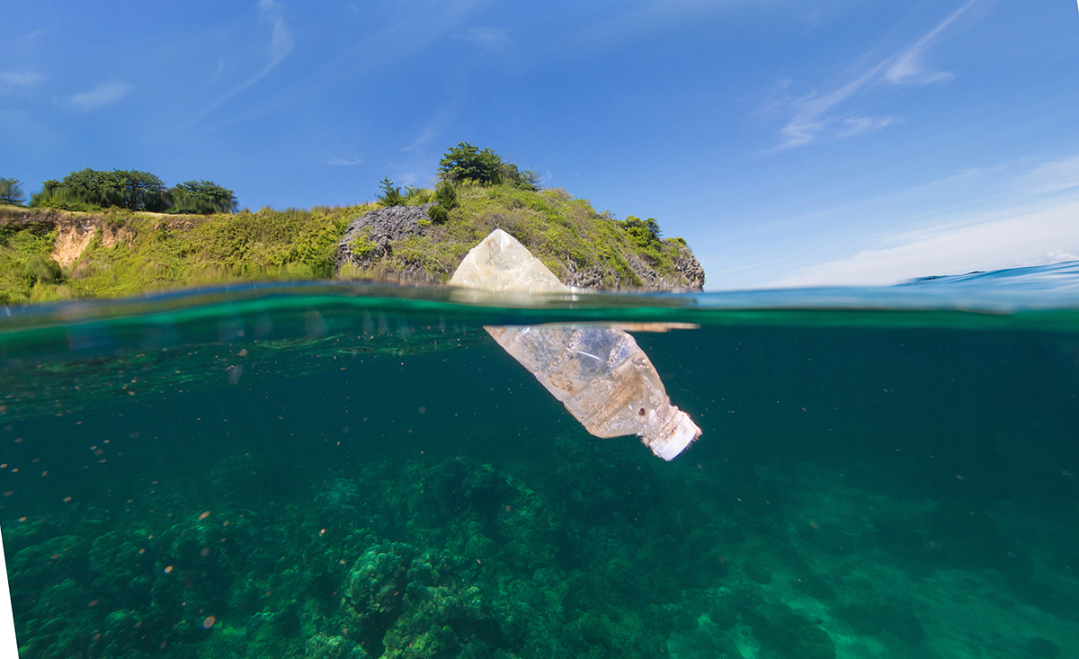 Botella de plástico flotando en el mar con una costa al fondo