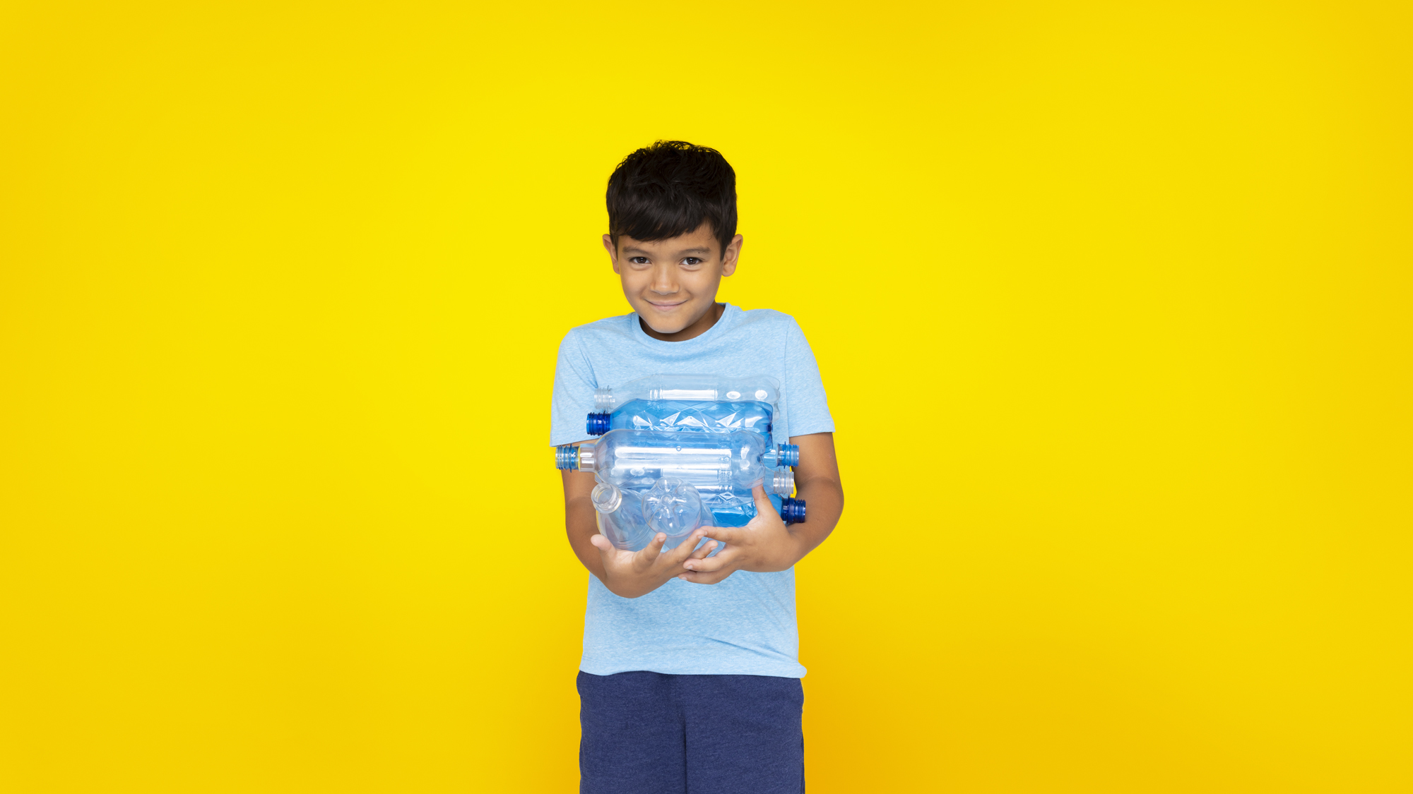 Boy yellow bckg holding PET bottles