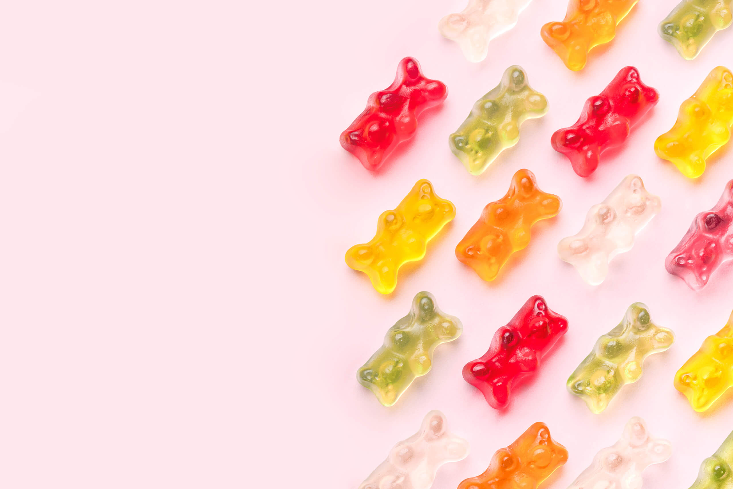 different colored gummi bears against a pink background